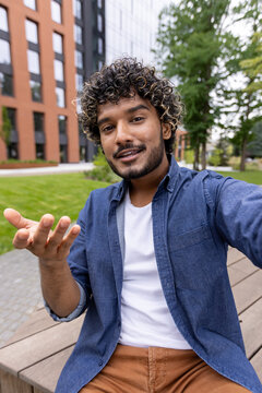 Student vlogger recording video call explaining online lesson with hand gestures outdoors on campus.