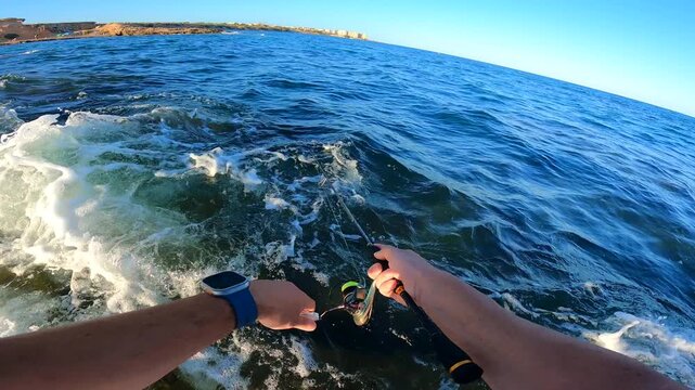 POV close up of angler working a sinking pencil lure with ultralight spinning rod over rocky coastal sea waves