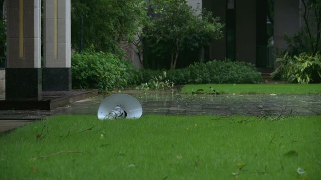 Fallen street lamp head lying on green grass after typhoon in rainy residential garden video with sound
