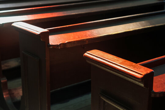 Rows of massive wooden pews painted in dark color in old catholic church, wooden benches in cathedral interior, religious background.