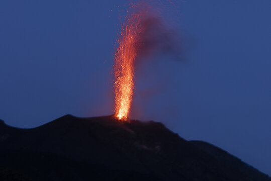 View of the Stromboli volcano erupting at night, with glowing lava and sparks shooting into the dark sky, Lipari, Sicilia, Italy.