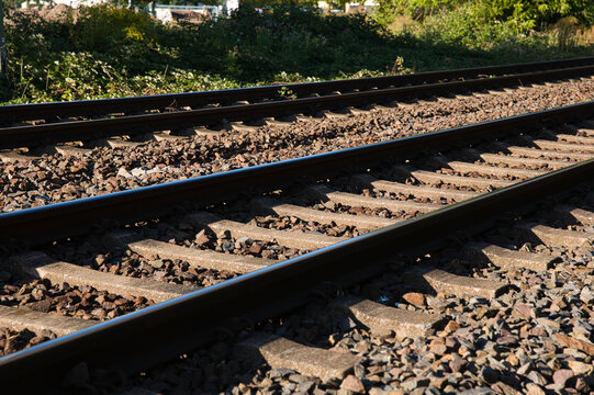 Multiple parallel railway tracks with steel rails, concrete sleepers and gravel ballast forming strong diagonal lines in warm sunlight.