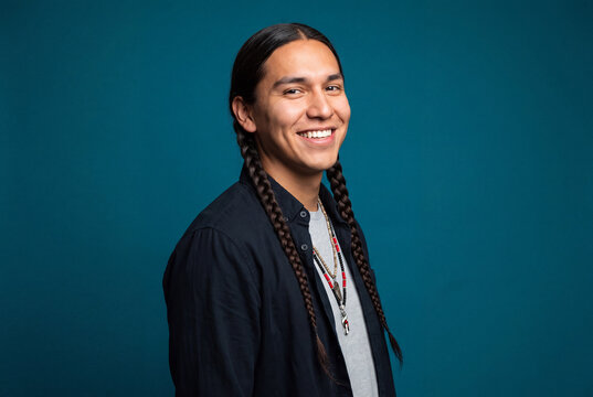 Portrait of smiling Native American young man with braided hair against blue background