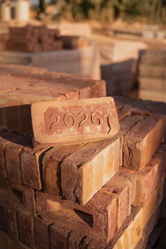 Red brick engraved with the year 2026 placed on a neatly stacked pile of red bricks at a construction site. Building materials, masonry, and new construction concept.