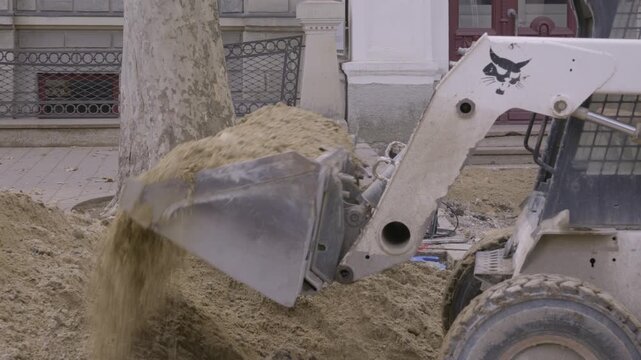 White skid steer loader scooping sand at urban street construction site