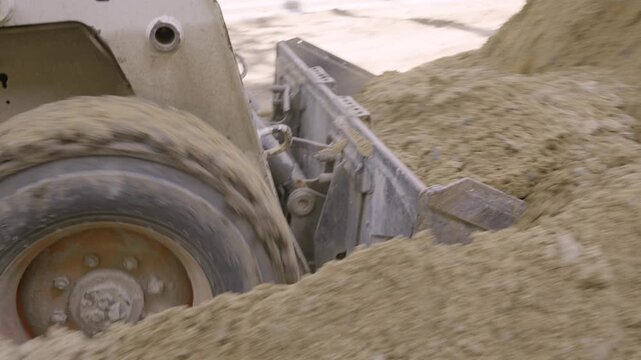 Close up of skid steer loader bucket pushing and dumping sand at construction site