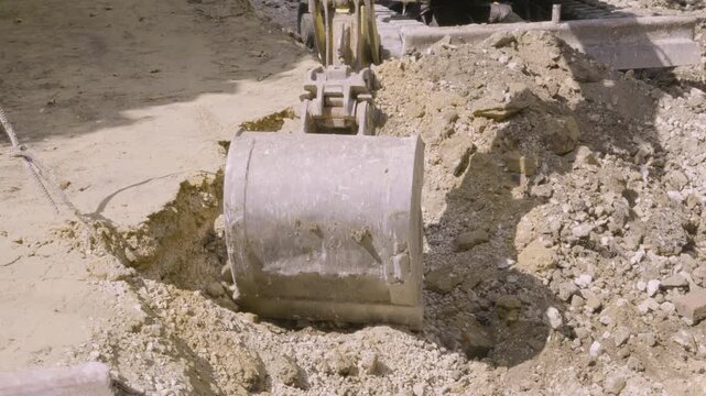 Mini excavator bucket digging earth and gravel at urban construction site