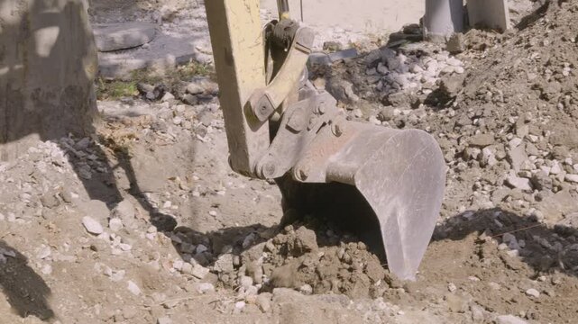 Close up of yellow excavator bucket digging dirt and rubble at urban construction site
