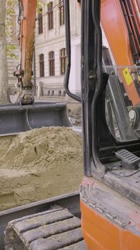 Vertical video of parked orange mini excavator on sand pile at urban construction site, city street road repair b-roll