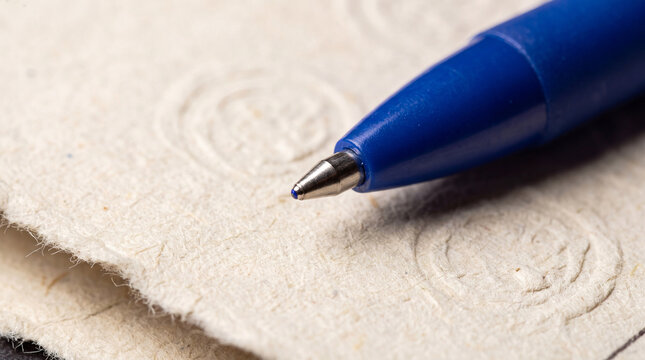 Blue ballpoint pen tip poised over textured handmade ballot paper, close up capturing the act of marking a vote and the democratic choice, responsibility, and civic participation