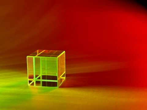 Transparent glass cube illuminated by vivid green, yellow and red light with colorful reflections, refractions and soft dramatic shadows on an abstract background