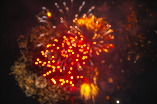 Red fireworks display captured out of focus against dark sky, creating soft glowing bursts and an abstract bokeh effect
