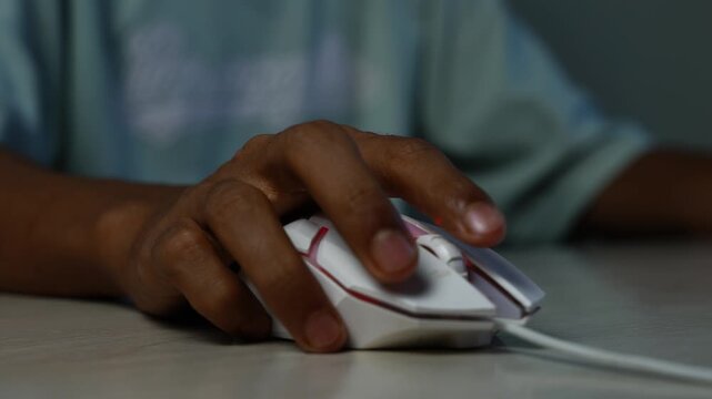 Hand using a wired computer mouse, Close-up of a person using a white wired computer mouse with pink accents on a desk, showing online work, gaming, or technology use.