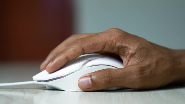 Hand using a wired computer mouse, Close-up of a hand using a white wired computer mouse on a desk, showing everyday technology, work, browsing, and online activity.