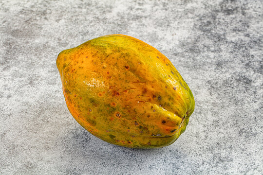 Ripe papaya with yellow green skin and brown spots on textured gray surface