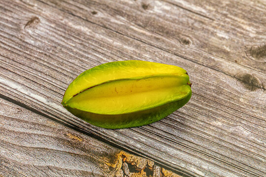 Fresh green and yellow starfruit slice on rustic weathered wood surface, shallow depth of field, natural lighting