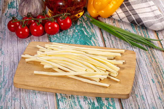 String cheese sticks on wooden cutting board with cherry tomatoes, yellow bell pepper, garlic, and saffron oil on rustic painted wood background