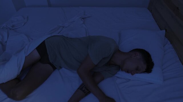 Man suffering from heat on a hot night, sweating and repeatedly changing position in bed during restless disturbed sleep