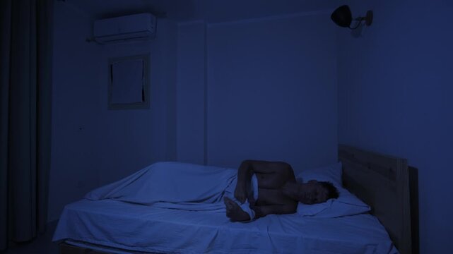 Sweating man unable to sleep during extreme heat, tossing and turning in bed on hot night while suffering from overheating