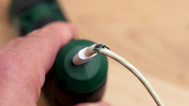 Damaged frayed electrical charging cable of green cordless power drill. Wire repair and maintenance concept