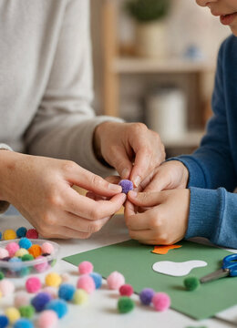 Adult and child assembling colorful pom poms for a craft project on a table with paper and scissors. Hands are focused on gluing a purple pom pom together in a cozy home setting.