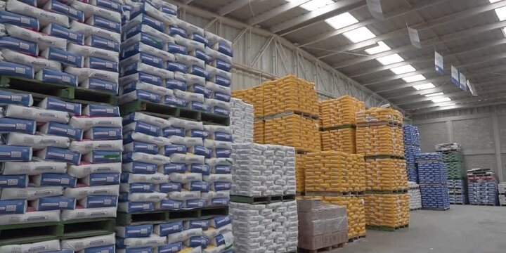 Large stacks of industrial cement bags stored on wooden pallets inside a commercial distribution warehouse facility featuring high ceilings and metal racks for heavy construction material