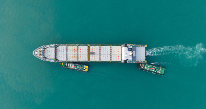 A bulk carrier is approaching the berth, with a tugboat pushing it alongside to load cargo.