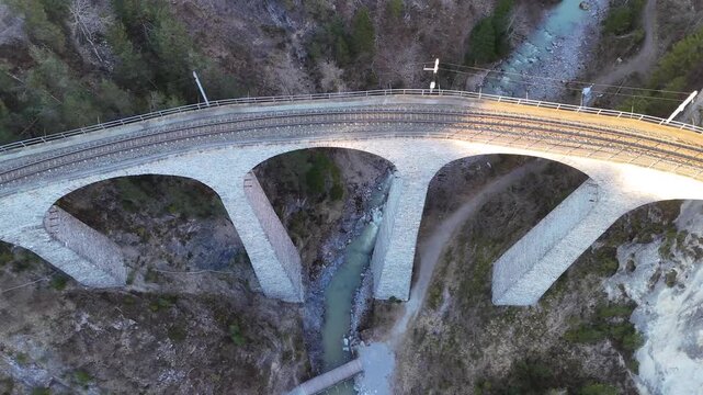 landwasser gorge river winds beneath viaduct arches filisur switzerland gravel trail follows streambed forested slopes catenary poles line track overhead aerial drone footage clear sky graubunden
