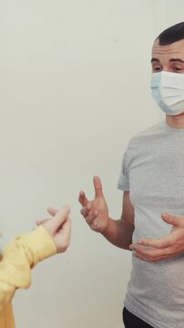 A man in a gray shirt talks to a woman wearing a yellow sweater. Both individuals are engaged in conversation while wearing masks, highlighting health precautions.