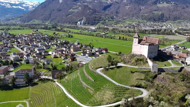 vineyard terraces switchback path hillside gutenberg castle round tower hilltop rhine valley farmland distant road balzers town rooftops snowcapped alpine peaks liechtenstein drone footage panorama