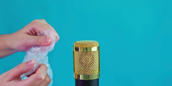 A person holds plastic bubble wrap near a golden sound recording device to create sensory audio experiences for digital listeners who enjoy listening to relaxing sounds and unique acoustic