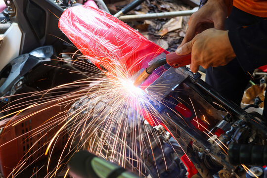 Welding worker repairs motorcycle frame with bright sparks in outdoor workshop