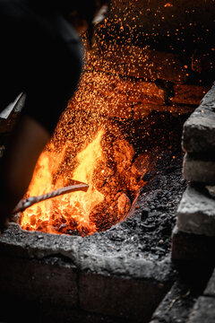 Blacksmith tending a blazing forge inside a brick workshop furnace, glowing orange flames and flying sparks