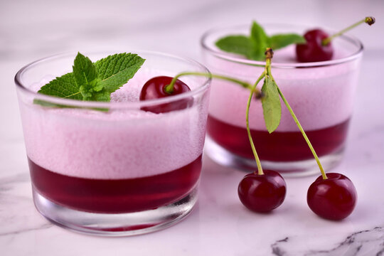 Cherry dessert with jelly and mousse in a glass on a black background. Close-up.
