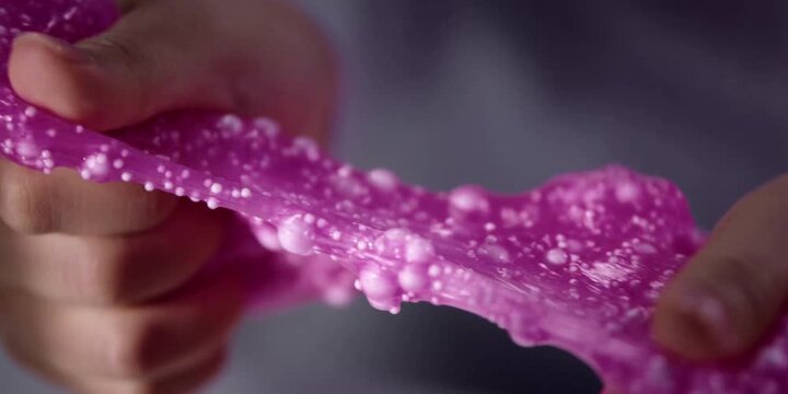 A pair of hands stretches a sticky purple substance filled with small polystyrene beads to demonstrate sensory tactile play activities and science experiments for children developing creative