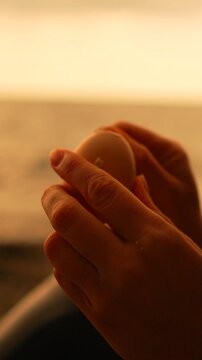 Egg peeling hands close up of fingers removing the shell from a boiled egg at the beach during golden hour