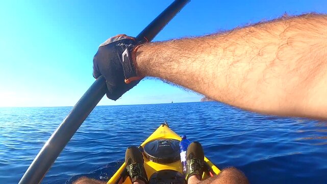 POV close up of man paddling a yellow kayak in open blue sea during a sunny calm day
