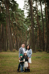 Happy family of four standing together and smiling in a tall pine forest, with plenty of copy space above. © Serhii