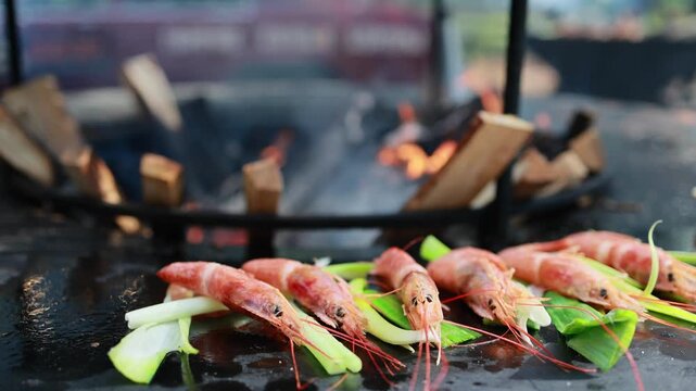 Fresh prawns with green onion cooking on hot black grill plate. Seafood barbecue preparation outdoors. Grilled shrimp with leek stems, healthy food and street food concept.