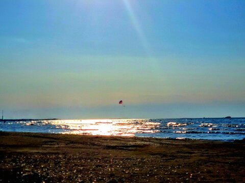 Silhouette of parasailing over calm sea at sunset