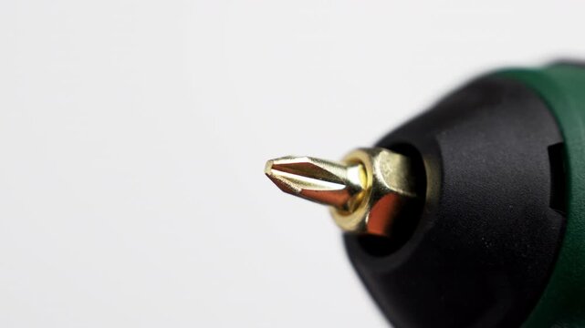 Gold screwdriver bit spinning with chuck of green cordless power drill against white background. Home improvement tools. Repair and maintenance equipment