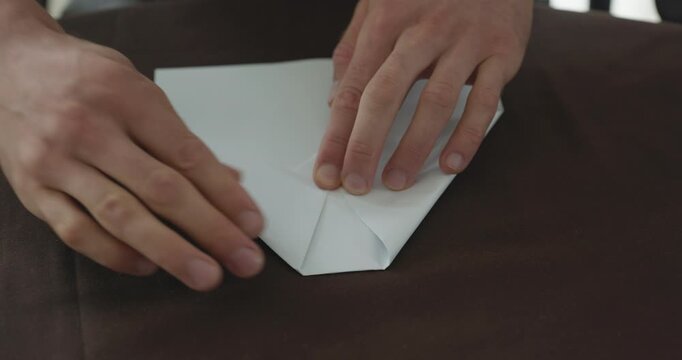 Close-up male hands fold sheet of paper making paper airplane. 4K 10-bit