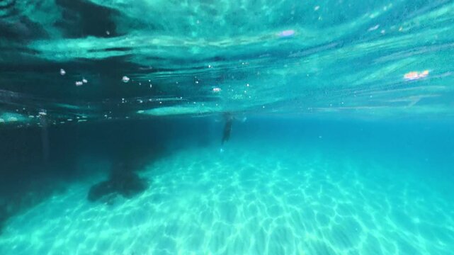 Freediver gliding gracefully over a sandy seafloor in crystal clear turquoise water. Low angle tracking shot.
