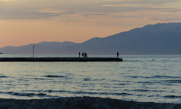 Silhouette of three people on a pier and a man fishing with Kefalonia in the background
