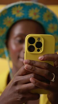 Smiling and happy Black American woman in stylish bob hat is taking photos with flashlight on her smartphone against yellow studio background. Global connectivity and tourism concept.