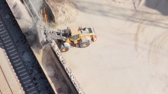 Yellow Wheel Loader Dumping Construction Material Into a Train Car at Daytime