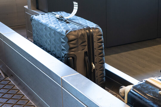 Black geometric patterned suitcase on baggage claim conveyor belt at airport terminal with modern design and polished metal surroundings