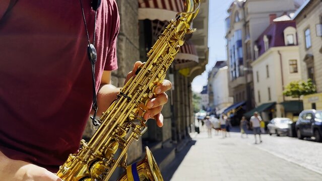 Male fingers of musician play the saxophone on summer day. Natural light reflects off metal surface, highlighting movement and rhythm. Scene captures live urban music and atmosphere street performance