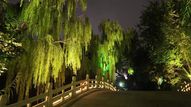Illuminated bridge and willow trees beside Daming Lake at night