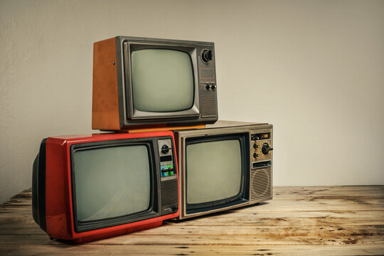 Pile of three retro old televisions with blank screen on wooden table on wall background.
